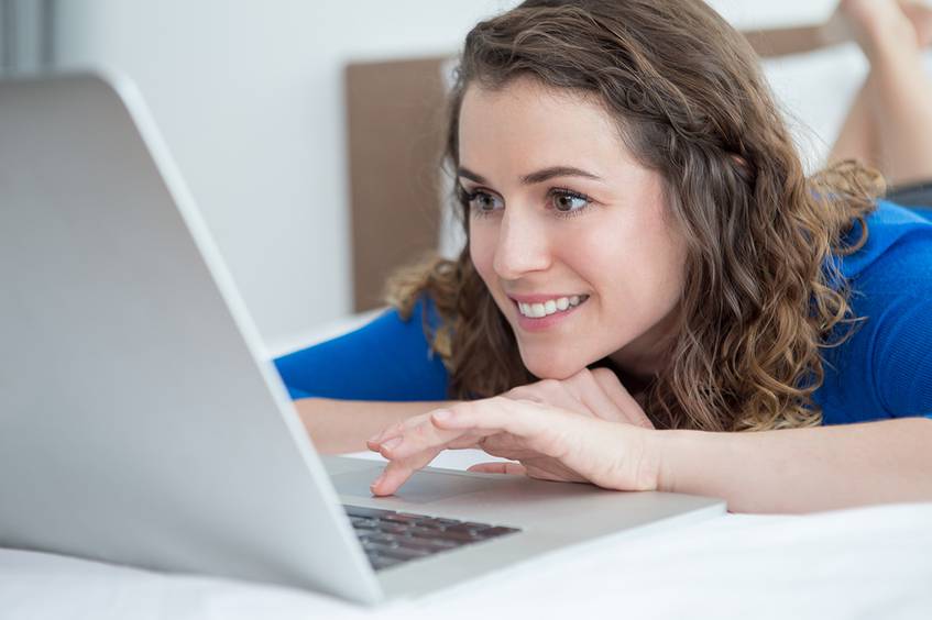 Woman lying down looking at a laptop screen.