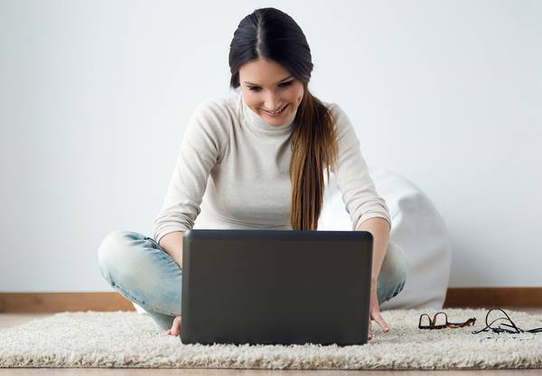 Happy woman using a laptop while lying on the floor.
