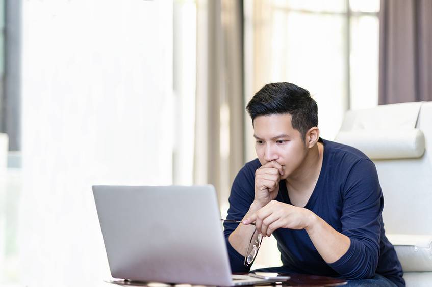 Man in front of a laptop appearing undecided