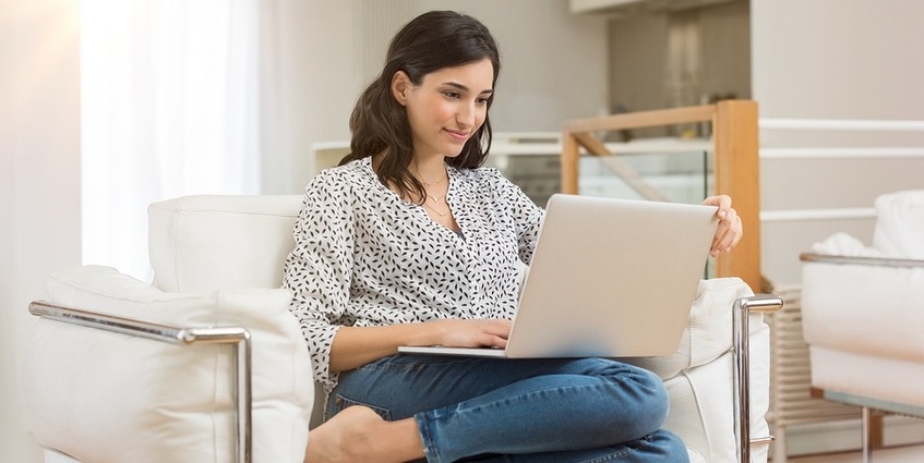 Woman sitting on a couch filling out an online form.